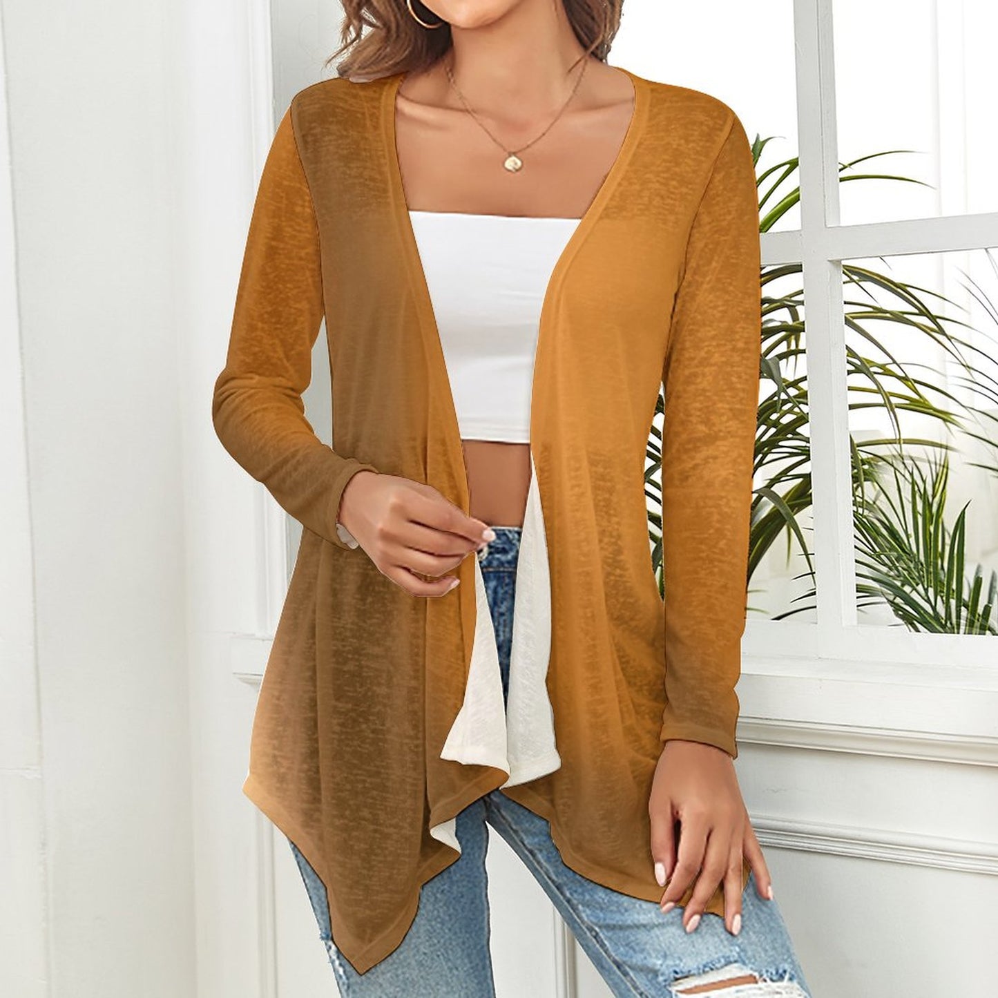 Woman wearing a gradient brown cardigan over a white top and blue jeans, standing indoors with a plant in the background. - Printspirationz