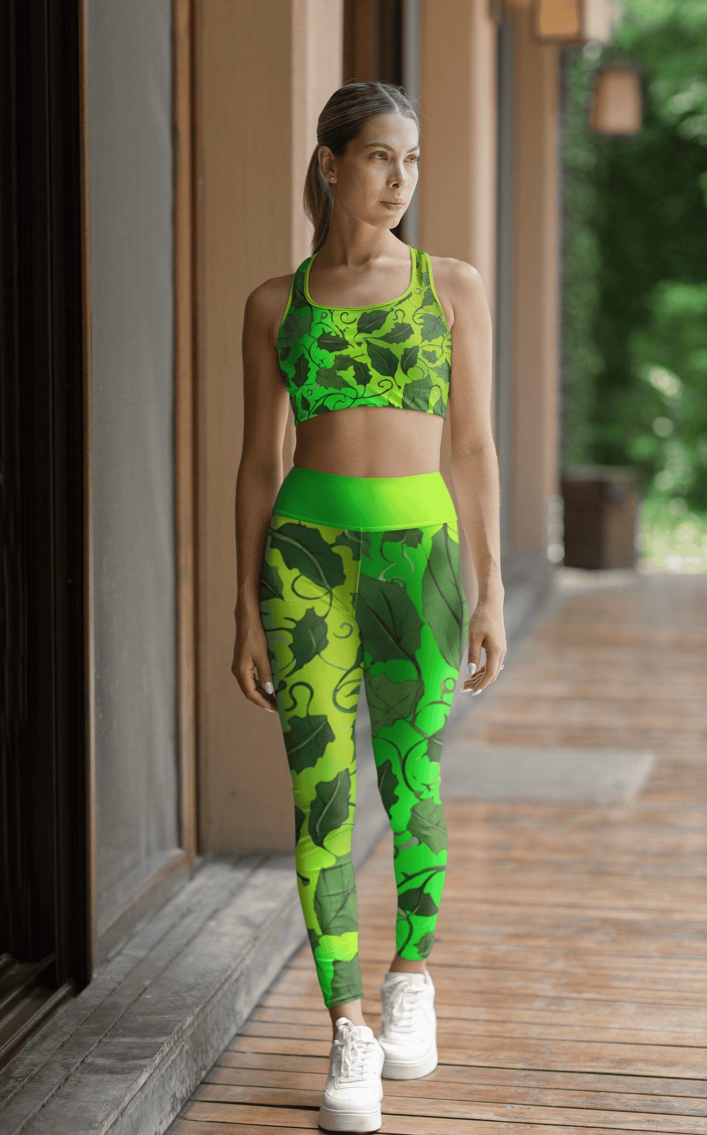 Woman wearing a  Vibrant Green Leaves sports bra and High Waist Yoga Leggings set on a wooden deck. - Printspirationz