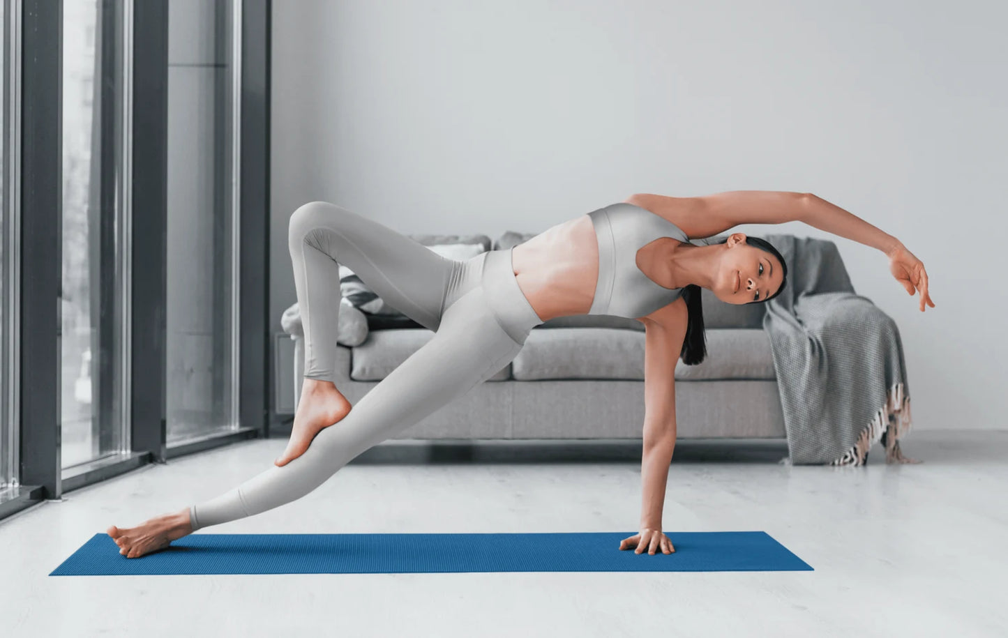 Woman practicing yoga wearing high waist yoga leggings in light gray on blue mat indoors