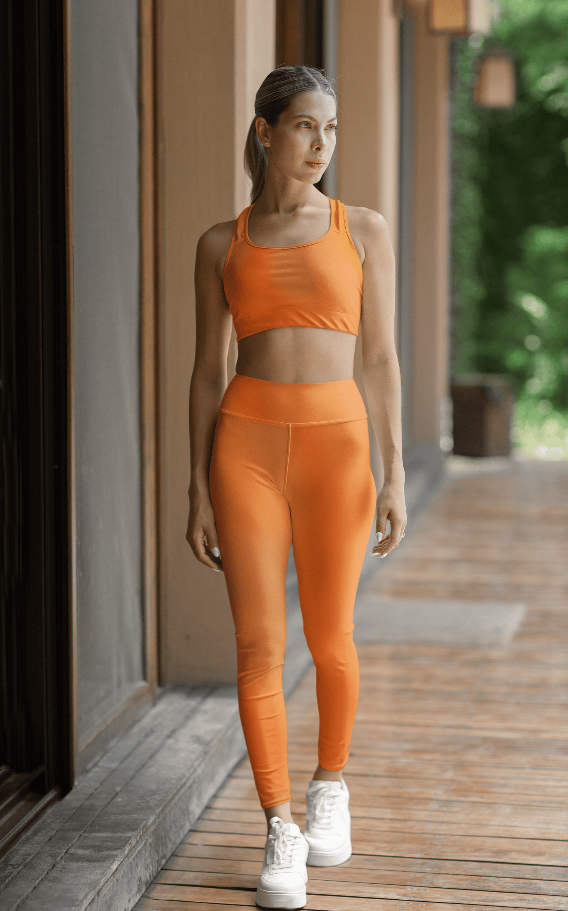 Woman wearing vibrant orange high waist yoga leggings and matching sports bra outdoors