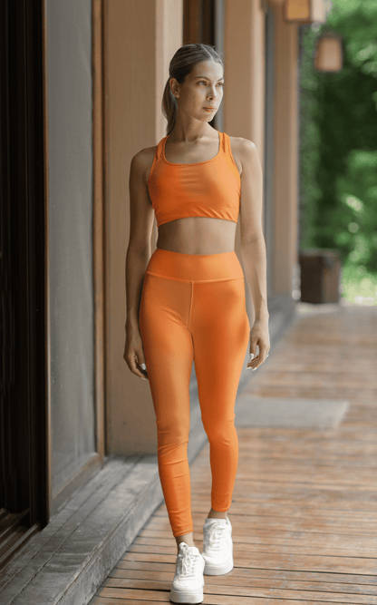 Woman wearing vibrant orange high waist yoga leggings and matching sports bra outdoors