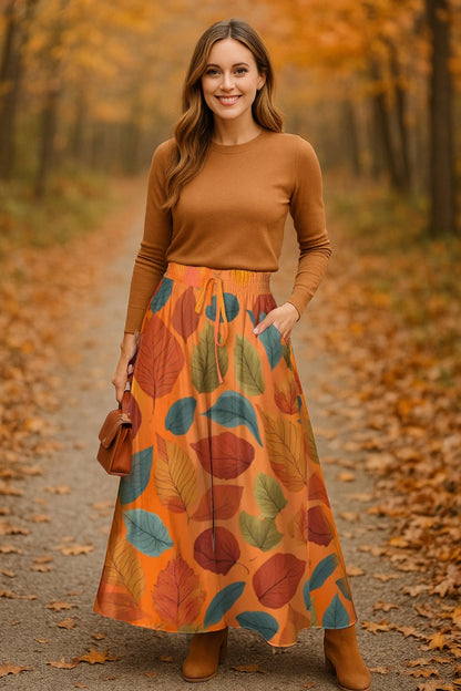 Woman in a brown sweater and long orange leaf-patterned skirt standing in an autumn forest.